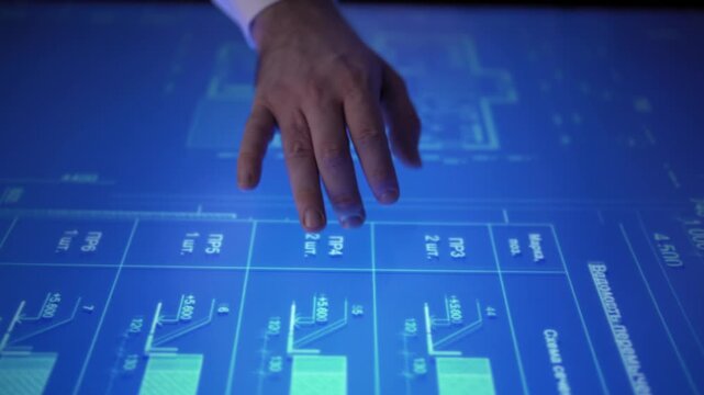 Man in an office moves a blueprint diagram on an interactive monitor with hand