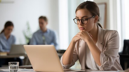 Pensive businesswoman wearing glasses looking at laptop screen in modern office