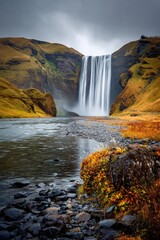 Obraz premium Dramatic waterfall cascading down a rocky slope in a landscape of autumnal colors