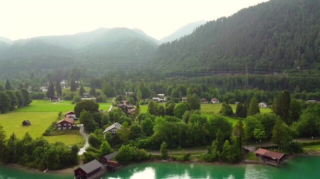 Drone view of alpine village by lake with forest and mountains