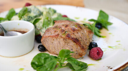 Dish with grilled veal fillet and roast beef sauce, garnished with basil, raspberries, and...
