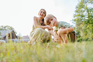 Fototapeta premium Mother sitting on grass with little son outdoors in countryside summer lifestyle