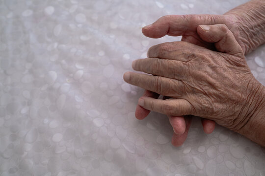 Elderly man showing tremors in his hands while resting on a table.