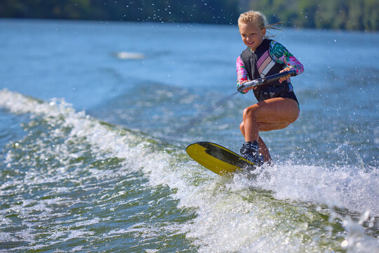 Smiling girl wakeboarder enjoying jump over lake waves. Concept of joy, childhood adventure, freedom, water sports, and playful energy.