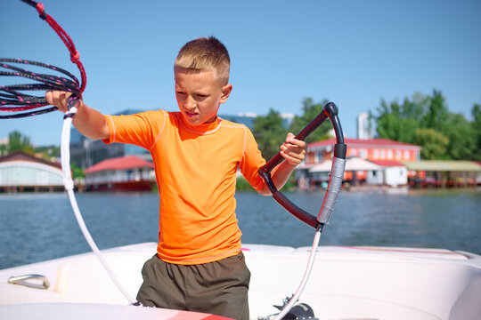 Boy in orange shirt preparing wakeboarding rope on boat with focus. Concept of training, discipline, summer sport lifestyle, and emotional concentration before water activity.