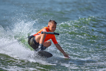 Wakeboard boy crouching close to water surface carving strong turn. Concept of precision, training, extreme water sports, control, youth power, and passionate motion.