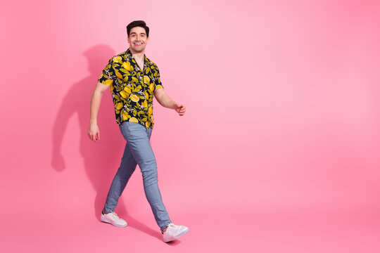 Young man in cheerful tropical shirt walking confidently against a pink background showcasing trendy summer style