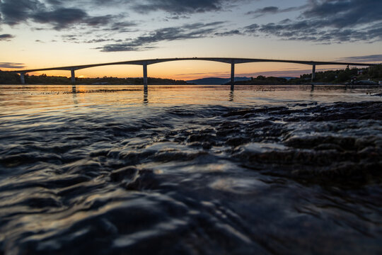 Bridge over troubled waters &ndash; a picturesque coastline with rocky shore, seaweed, and golden sky during evening light.