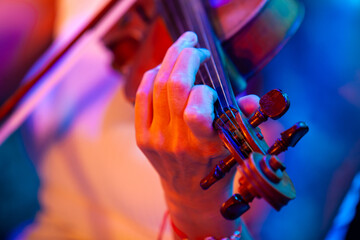 Close-up of woman hands playing violin under colorful stage lights