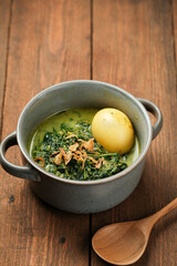 Cassava leaves cooked with coconut milk and delicious spices in a bowl on a wooden base