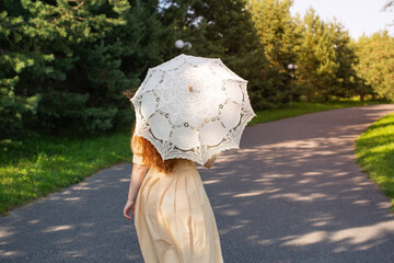 A woman walks through the park. A person in a yellow dress with an openwork umbrella is walking. The woman moves away in the frame.