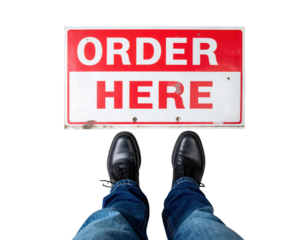 A red-and-white "ORDER HERE" floor sign positioned in front of a pair of black shoes clad in blue jeans.