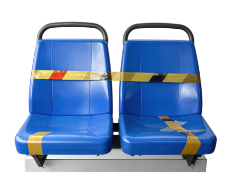 Two blue molded plastic public-transport seats on a metal base, taped off with yellow-and-black caution tape.