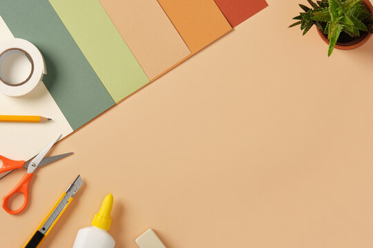 Supplies for paper art hobby: scissors, craft knife, pencil, eraser, colored paper on beige background. Space for your text.