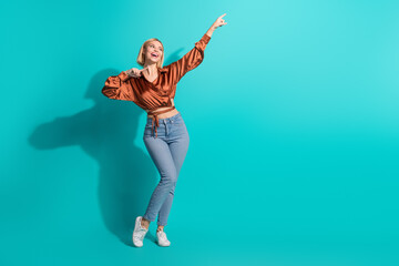 Happy young woman in a stylish blouse on a teal background feeling joyful and pointing up with a...