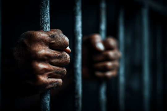 Close up of hands gripping prison bars dark background showing confinement and despair