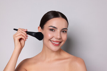 Fototapeta premium Beautiful woman applying makeup with brush on light grey background