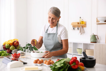 Senior woman cooking salad at white marble table in kitchen