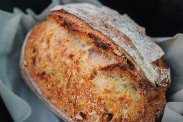 A rustic loaf of sourdough bread, beautifully scored and baked, resting on parchment paper. It has a golden-brown crust and a fluffy interior.