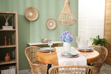 Stylish setting with plates and vase of flowers on wooden table in dining room. Interior design