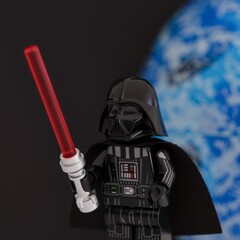 Naklejka premium Tambov, Russian Federation - November 14, 2024 Lego Darth Vader minifigure with red lightsaber against black background with a blue planet