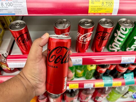Hand Holding Red Coca Cola Zero Sugar Can in Supermarket Aisle