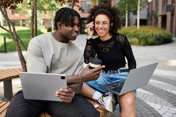 Creative urban couple enjoys remote work while sharing a coffee together in summer sun