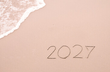 2027 year handwritten with ocean waves on a sandy beach. New Year 2027 concept