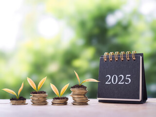 2025 desk calendar and plants growing up on stack of coins. The concept of business growth,...