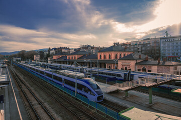 Modern passenger train at a station, city buildings and cloudy sky backdrop, embodying transit efficiency and urban connectivity.