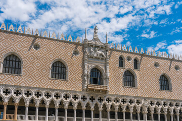 Obraz premium Ornate building facade featuring Gothic arches, stone lattice, diamond patterned brick, under a blue sky with cloud accents.