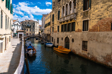 Venetian canal scene featuring boats, historic buildings with arched windows, and a bridge under a...