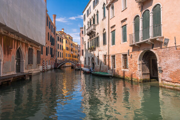 Venetian canal reflecting colorful buildings under a bright sky. Traditional architecture is seen along the waterway.
