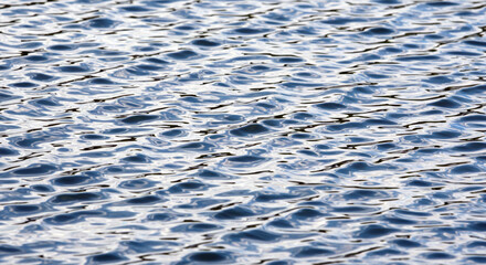 Abstract close up view of shimmering blue water surface with small ripples and light reflections creating a dynamic textured pattern