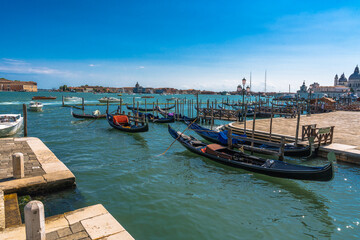 Obraz premium Venice Canals: Gondolas line the waterfront under a clear blue sky in Venice, Italy. Classic Venetian scene.