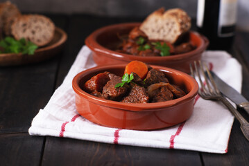 Beef meat stewed with carrots and spices in ceramic pot.