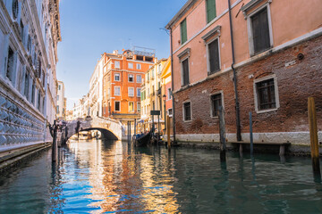 Venetian Canal Scene: Reflections of colorful buildings along a calm canal with a gondola and a small bridge.