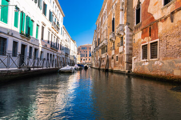 Venetian Canal Scene: A picturesque canal winds through aged buildings under a clear sky in Venice, Italy. Gondolas gliding along.