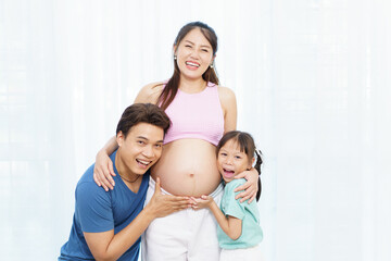 Asian family with pregnant mother, father, and daughter hugging belly with love and joy.