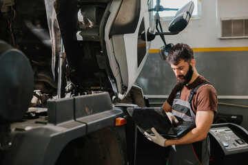 Auto mechanic using laptop while repairing truck in garage