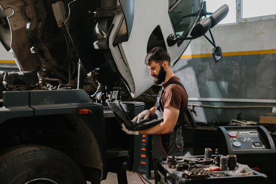 Mechanic using laptop diagnosing truck malfunction in garage