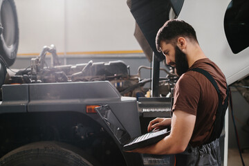 Mechanic using laptop diagnosing truck engine problem in garage