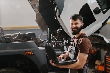 Mechanic using laptop diagnosing truck engine problems in garage