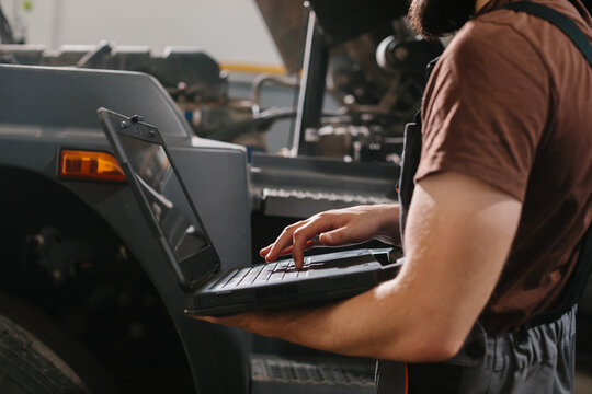 Mechanic using laptop for truck diagnostics in repair shop - Powered by Adobe