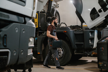 Auto mechanic carrying toolbox walking to repair truck in garage
