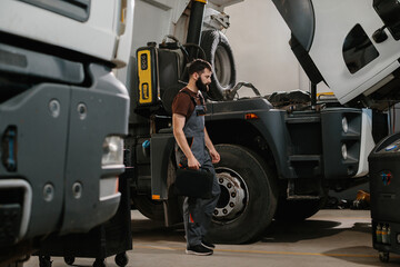 Auto mechanic carrying toolbox and walking towards truck in repair shop