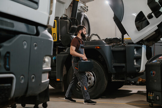 Auto mechanic carrying toolbox walking to repair truck in garage