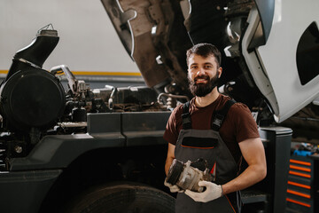Mechanic holding truck part, repairing a big rig in a garage