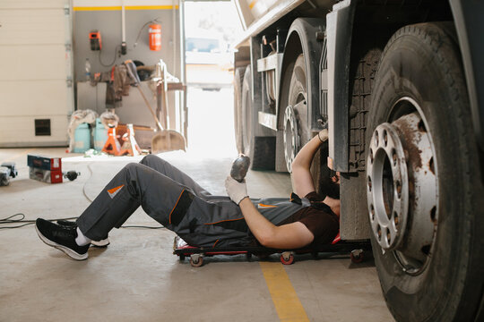 Mechanic lying down and repairing truck wheel in garage