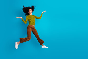 Fototapeta premium Enthusiastic young woman jumps against blue background, showcasing vibrant energy and trendy style, perfect for promoting positivity